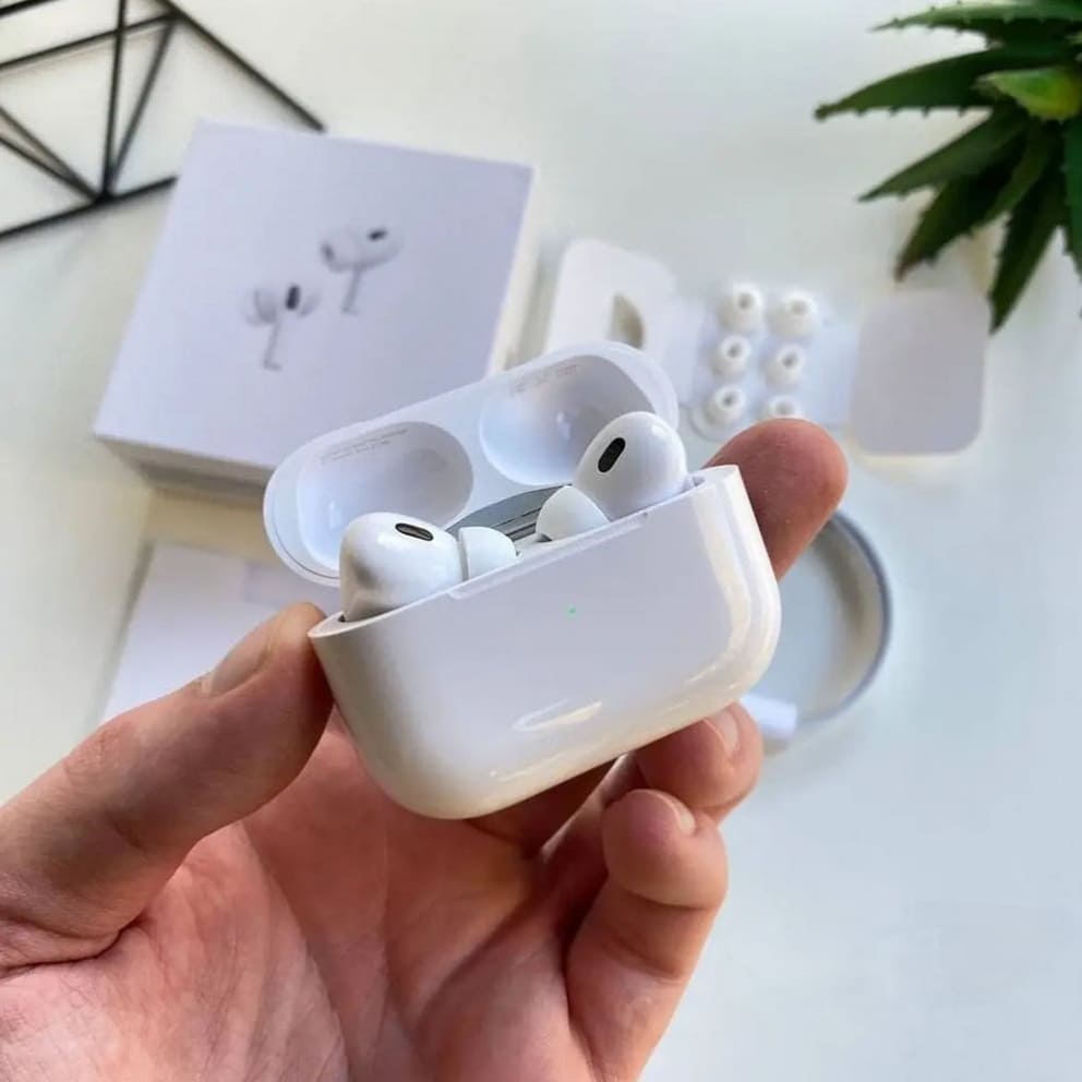 White Adipods Pro 2 wireless earbuds in a charging case held by a hand on a light background.
