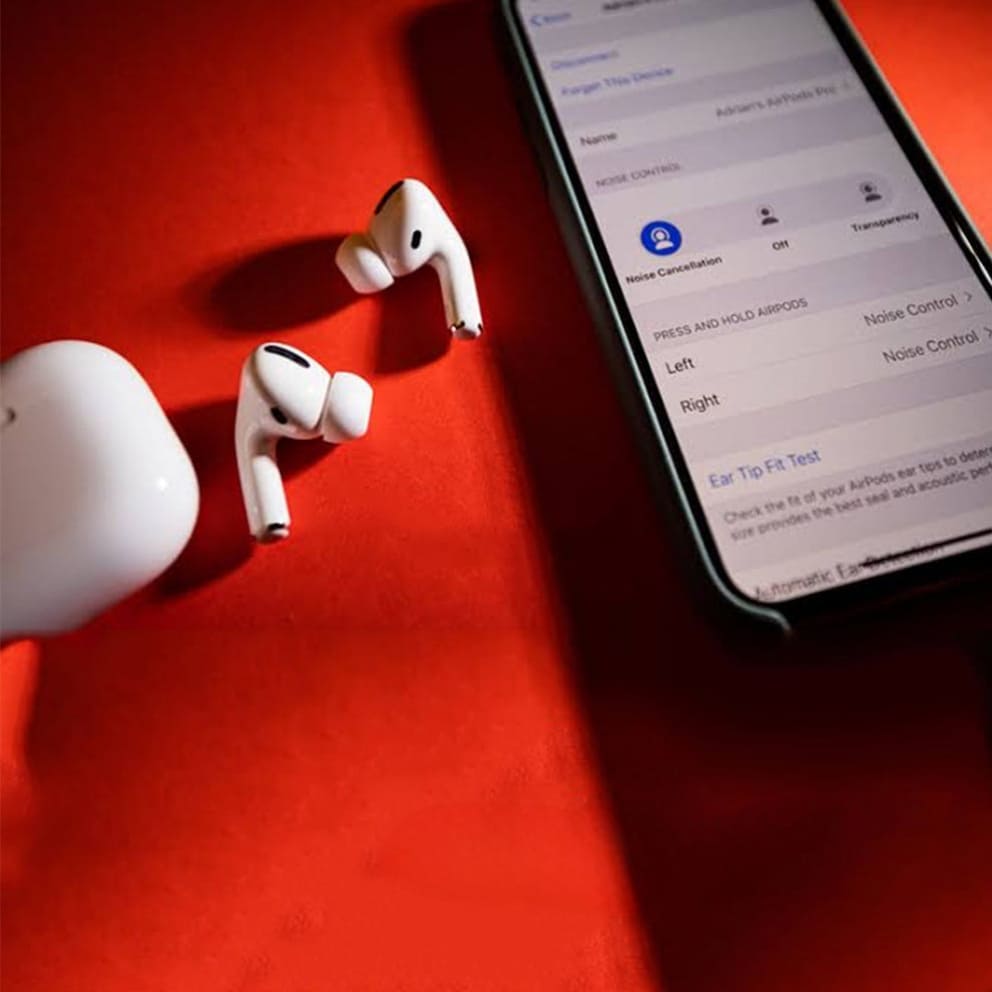White Adipods Pro 2 wireless earbuds on a red surface with a smartphone displaying an app interface.