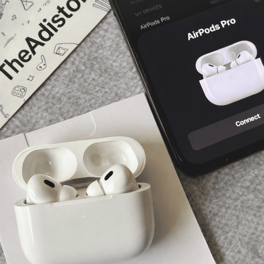 Adipods Pro 2 in charging case with smartphone displaying connection screen on a gray surface.