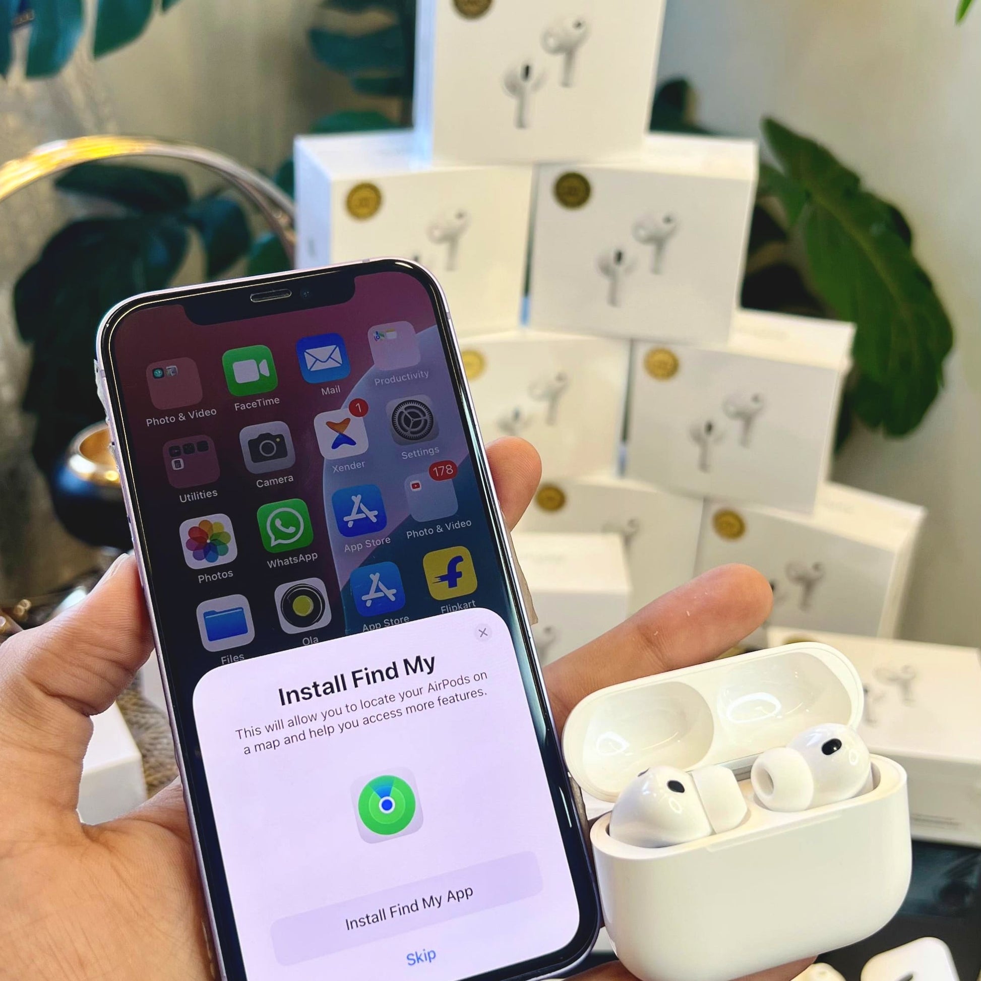 Person holding a smartphone with an app installation screen, next to Adipods Pro 3 wireless earbuds in a case, with multiple white boxes in the background.
