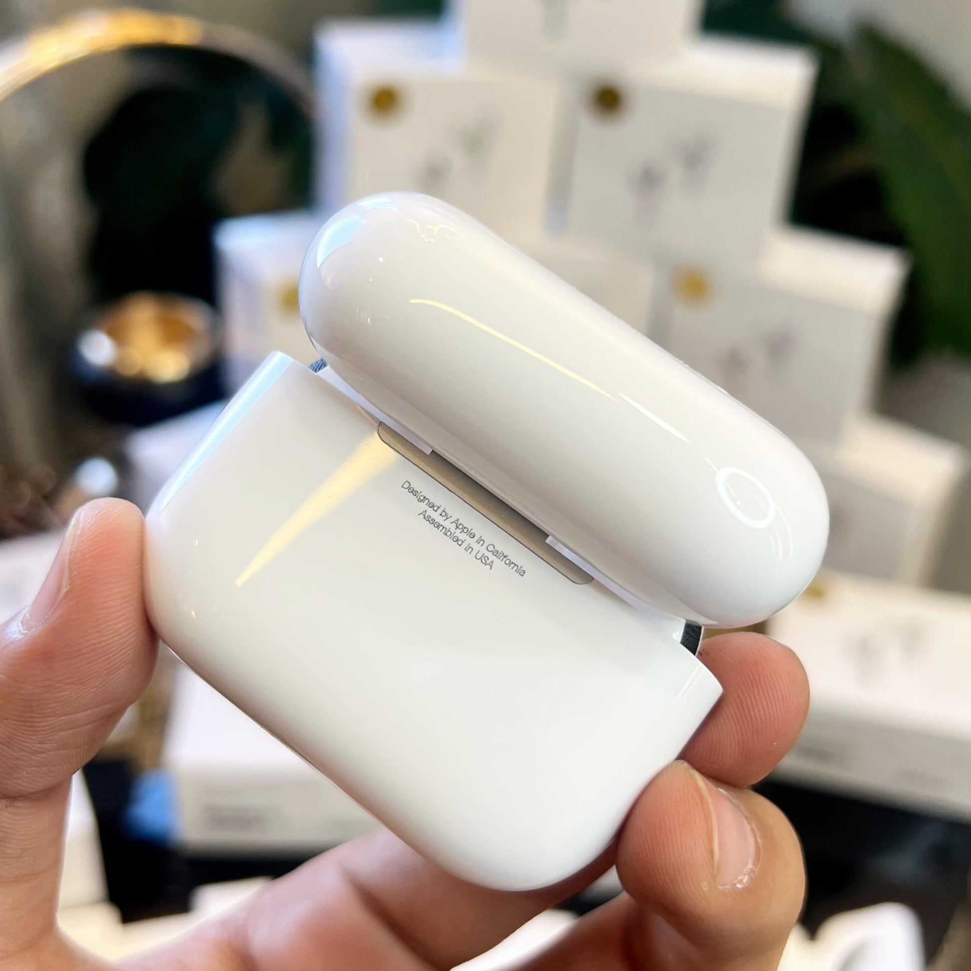 White Adipods Pro 3 wireless earbuds in a case held by a hand with blurred product packaging in the background.