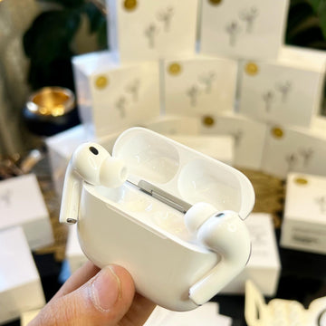 White Adipods Pro 3 wireless earbuds in a charging case held by a hand with a blurred indoor background.