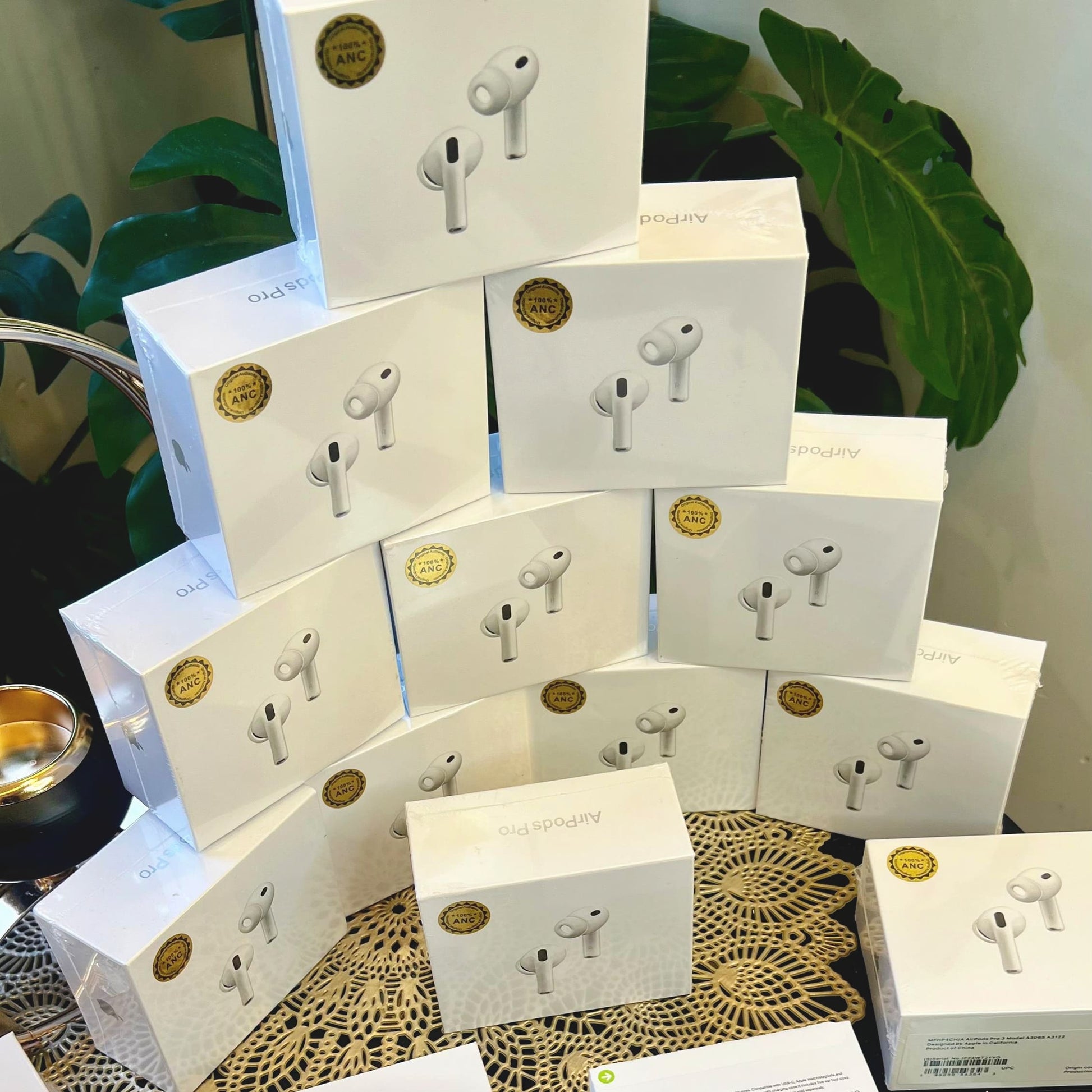 Multiple boxes of Adipods Pro 3 wireless earbuds stacked on a surface with green plants in the background.