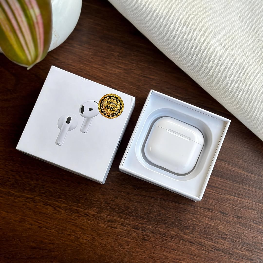 White Adipods Pro 4 wireless earbuds in an open box on a wooden surface with a plant and fabric in the background.